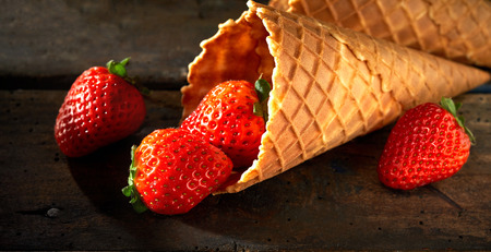 Tasty fresh ripe red strawberries in a cornet or waffle ice cream cone spilling onto a rustic wood counter in banner formatの写真素材