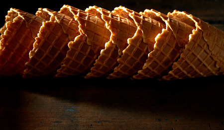 Stacked empty cornets or ice cream waffle cones on shadowy dark rustic wood with highlights for texture and copy spaceの写真素材