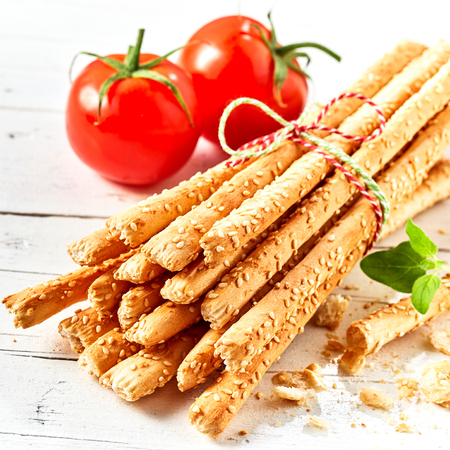 Bunch of grissini breadsticks in close up with tomatoes against white wooden backgroundの写真素材