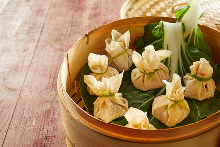 Traditional Asian fresh dim sum dumplings served on green cabbage leaves in bamboo basketの写真素材