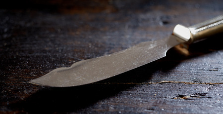 Old vintage silver butter knife lying on a dark rustic wood table view at a low angle with focus to...