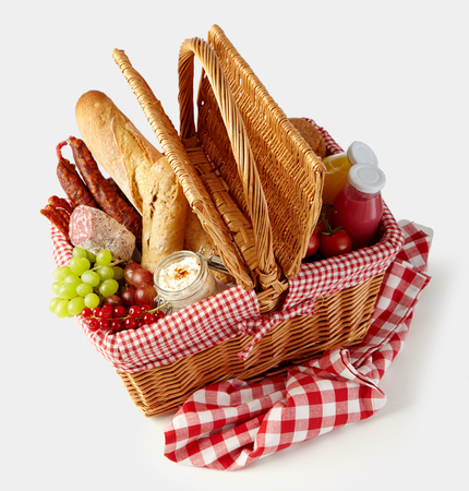 Fresh tasty food in a wicker picnic basket isolated on white with fruit, juice, spicy sausages and crusty bread viewed high angleの写真素材