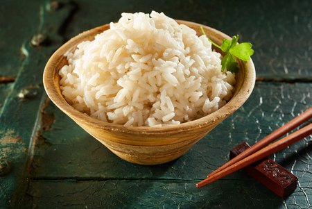 Side View Close Up Profile Still Life of Small Wooden Bowl of White Rice with Chopsticks and Garnish on Wooden Table with Cracked Painted Surfaceの写真素材