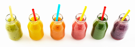 Panorama of healthy fresh vegetable and fruit smoothies in clear glass bottles with straws viewed top down isolated on white for advertisingの写真素材