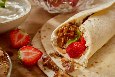 Homemade strawberry and walnut wraps with fresh whipped cream and mint in a close up view of the rolled end surrounded by ingredientsの写真素材