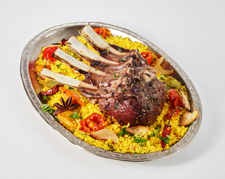 Spicy seasoned roasted Oriental lamb chops on couscous, tomato and onions served on a metal plate viewed high angle over whiteの写真素材