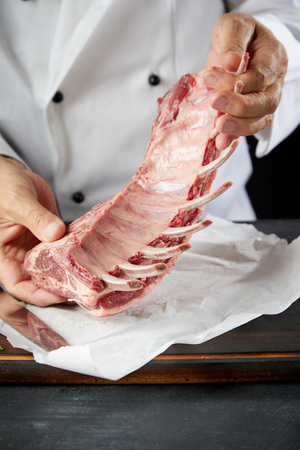 Butcher or chef handling a raw rack of lamb with bone-in chops during preparation for cooking in a close up view of his handsの写真素材