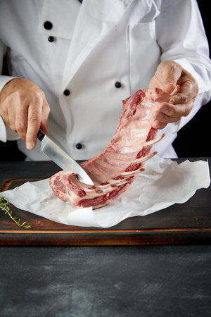 Chef preparing raw lamb chops for cooking separating the rack of lamb into portions for roasting using a knife in a close up view of his hands with copy space belowの写真素材