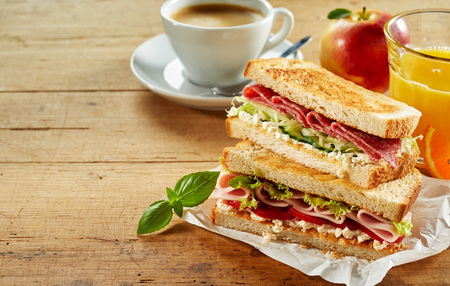 Tasty cafeteria breakfast with assorted toasted meat sandwiches, freshly squeezed orange juice, apple and cup of coffee on a rustic wood table with copy spaceの写真素材