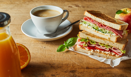 Tasty meat sandwiches on toasted white bread served with a fresh apple, bottle of orange juice and coffee for breakfastの写真素材