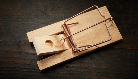 High angle of wooden mousetrap bar with cocked spring, sitting on dark floor without a baitの写真素材