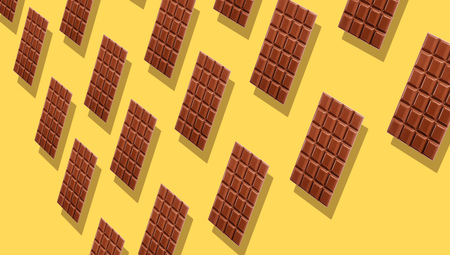Milk chocolate tablets duplicating on yellow background with shadows viewed in perspective, and full frame.の写真素材