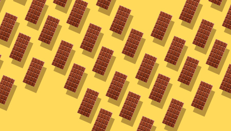 Pattern of small duplicating milk chocolate tablets on yellow background with shadows, viewed from above in full frameの写真素材