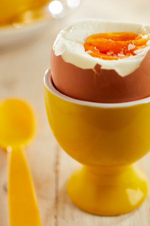 Close-up on open soft-boiled organic egg in yellow ceramic eggcup served with plastic spoonの写真素材