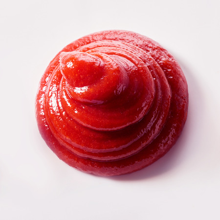Top down view of a decorative twist of fresh homemade tomato sauce or ketchup on whiteの写真素材