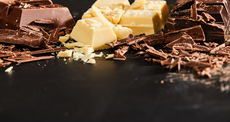 Close-up of pieces of white and milk chocolate with shavings on kitchen table as cooking ingredients. Copy space on dark backgroundの写真素材
