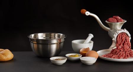 Meat minced through old manual grinder and other cooking ingredients in white bowls for making meat...