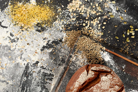 Assorted grain seeds with a freshly baked crusty loaf of bread and flour on a messy kitchen counter...