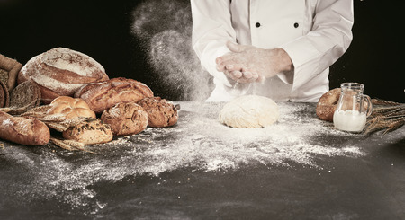 Baker clapping his hands in a cloud of flour as he prepares the dough for his speciality breads...