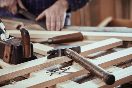 Carpenter working in his workshop with freshly planed planks with old hand tools and nails in the...