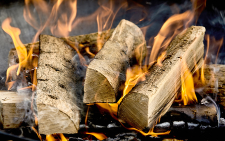 Dried logs of wood burning in a barbecue or home hearth on a bed of coals with fiery orange flames...