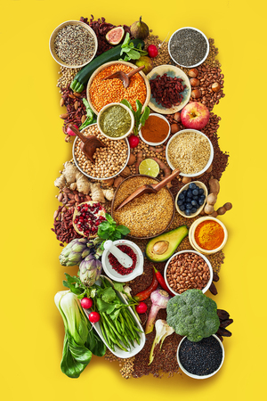 Large assortment of fresh fruit, vegetables and spices with pulses, pomegranate, avocado, artichoke, seeds, endive, fig and lemon on a colorful yellow background framing the foodの写真素材