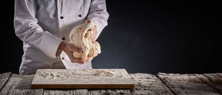 Baker of chef kneading a large portion of dough with his hands during preparation over a floured...