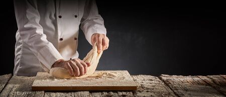 Hands of a male chef, cook or baker kneading dough on a cutting board over on old rustic wooden...
