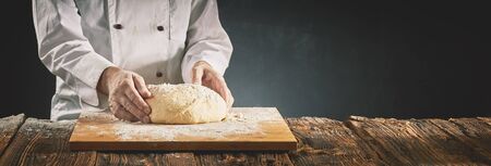 Chef in a pizzeria or baker preparing a mound of raw dough on a floured wooden board on a rustic...