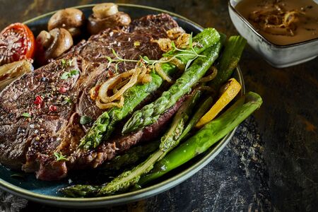 Fresh green asparagus spears served with a thick juicy grilled beef steak, mushrooms and tomato for a gourmet seasonal dinnerの写真素材
