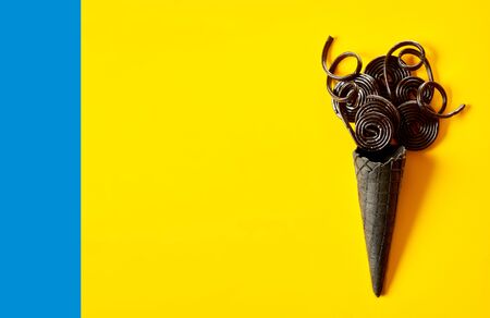 Creative ice cream in a cone concept on yellow with twirled coils of liquorice in a grey cornet over...