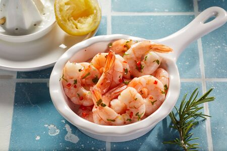 Spicy chili seafood starter of fresh scampi tails served with herbs and lemon juice in a white pannikin on blue tilesの写真素材