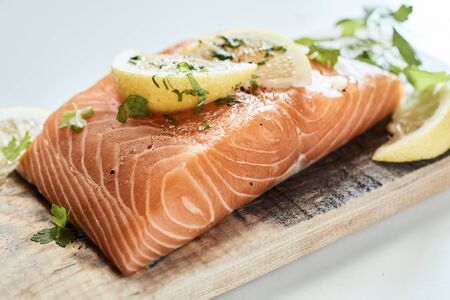 Close up on a thick raw fillet of salmon seasoned with fresh herbs and lemon ready for grilling on a...