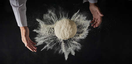 Mound of freshly made dough with flour burst and the hands of a chef of cook in a pizzeria or bakery...