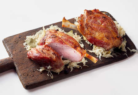 Roasted German Eisbein or pork hocks on a bed of sauerkraut served on a rustic chopping board on whiteの写真素材