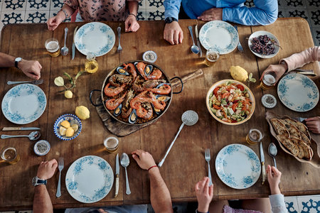 From above of crop faceless company of friends sitting at table with traditional seafood paella...