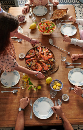 From above of crop faceless company of friends sitting at table with traditional seafood paella while spending weekend together in Spanish restaurantの写真素材