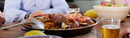 From above of crop faceless company of friends sitting at table with traditional seafood paella while spending weekend together in Spanish restaurantの写真素材