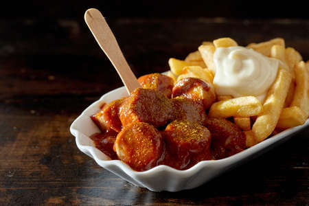 Closeup of appetizing grilled chopped sausages with barbecue sauce served with French fries and mayo...