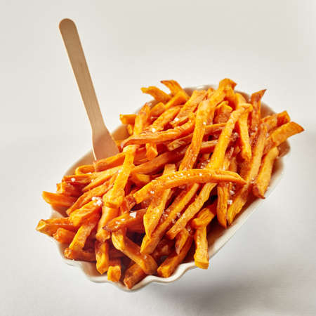 From above of yummy fried potato sticks with condiments and wooden fork in porcelain bowl on light...