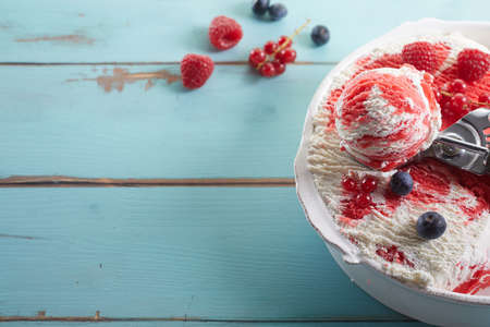 High angle of bowl of homemade frozen yogurt ice cream topped with red syrup and decorate with blueberries, raspberries and red currantsの写真素材