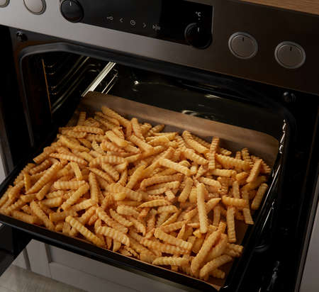 From above pile of crispy crinkle fries ready for lunch placed on tray in open oven