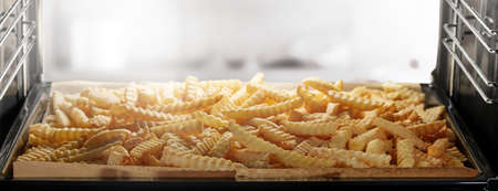 Wide angle of heap of yummy crinkle cut fries roasting on tray inside modern oven in kitchen