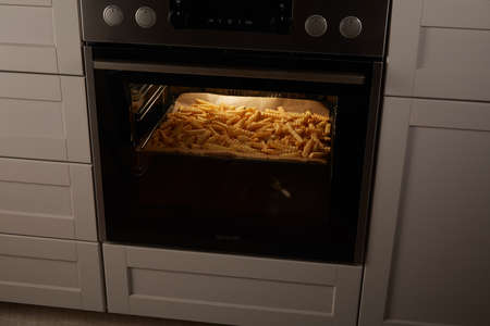 High angle of heap of crinkle cut fries baking in hot contemporary oven in kitchen