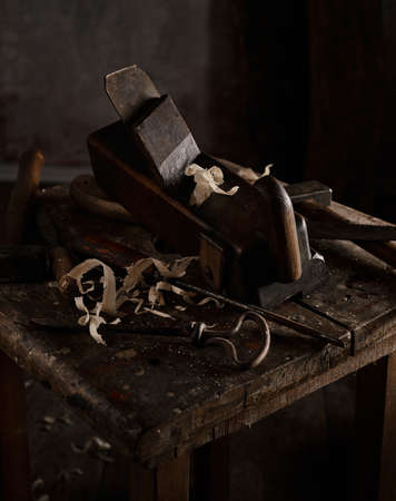 High angle of various aged carpentry instruments placed on shabby lumber table in dark joinery