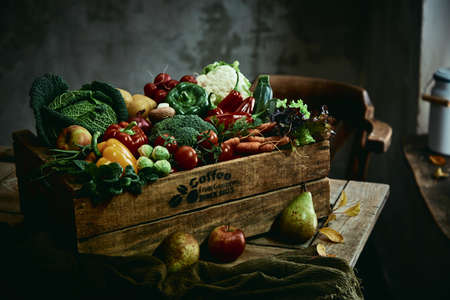 Lumber box with various ripe fruits and vegetables placed on rustic table in grungy roomの写真素材