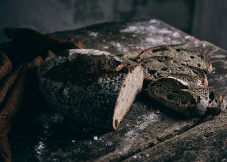 High angle of pieces and loaf of cut rye bread placed near brown napkin on lumber table in dark...