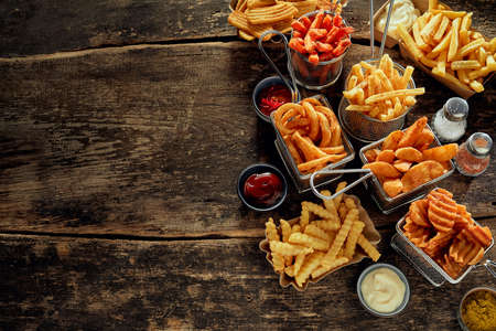 High angle of different types of French fries placed near roast chicken served with lettuce leaves and sauces on tableの写真素材