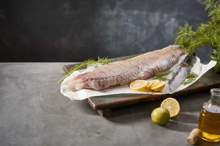 Raw pollock fish fillet with sliced lemon and fresh dill placed on table with olive oil during the...