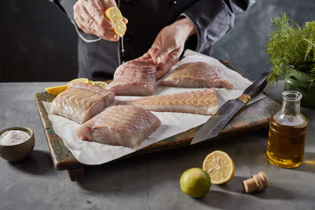 Crop unrecognizable cook seasoning raw fish fillet with lemon juice while preparing healthy meal in...